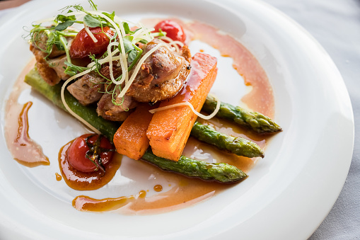 Roasted duck in slices with thyme in port wine sauce, served with cherry tomatoes, sliced potatoes, carrots and asparagus.