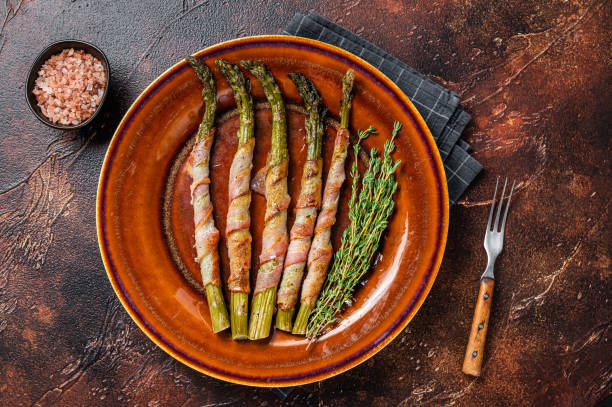 istock Grilled green asparagus wrapped with bacon on a plate. Dark background. Top view 1341736472