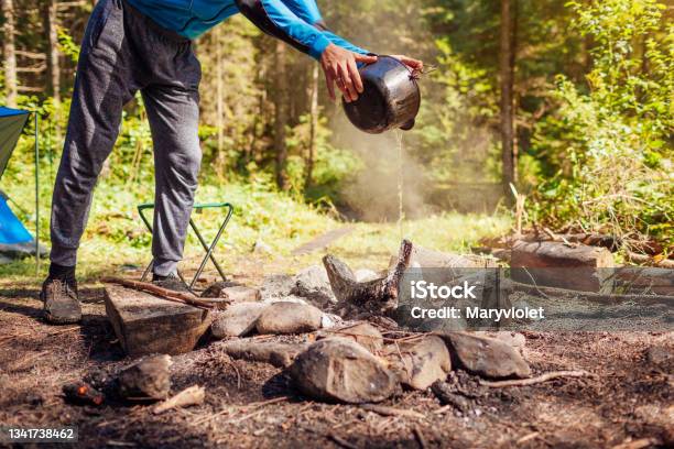 Man Extinguishing Campfire With Water From Cauldron In Summer Forest Put Out Campfire Traveling Fire Safety Rules Stock Photo - Download Image Now