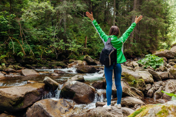 istock Traveler hiker with backpack raising arms by mountain river waterfall in Carpathian forest feeling happy. 1341738466