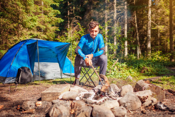 istock Man relaxing by campfire in forest sitting next to tent. Summer camping. Traveling alone 1341738804
