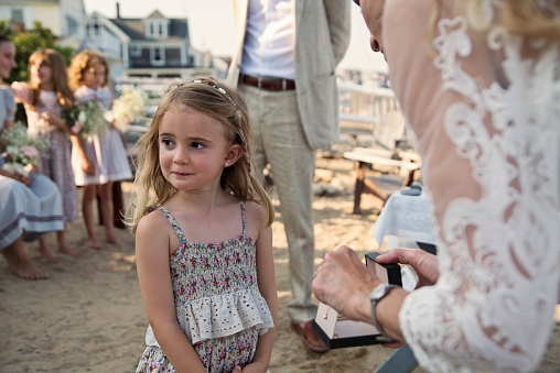 Bride giving gift to daughter during small intimate wedding ceremony at the family beach house. Bride and groom are in their forties. There are no other guests invited because of COVID. Horizontal waist up outdoors shot.