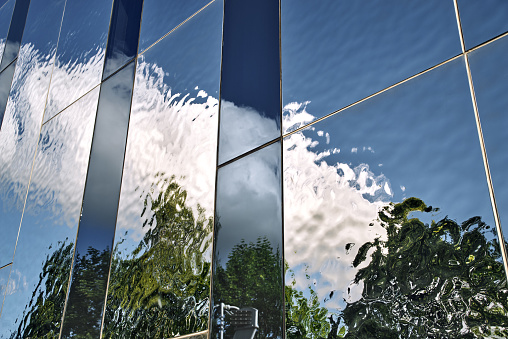 johannesburg, South Africa - july 06 , 2021:  clouds and trees reflecting off of a glass paneled building midday jhb cbd