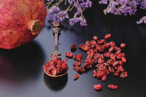 melograno maturo e anardana secca biologica o semi essiccati al sole di frutta di melograno su sfondo scuro in cucchiaio vintage cooper di design orientale. concentrati sul primo piano. erbe e spezie biologiche - arils foto e immagini stock