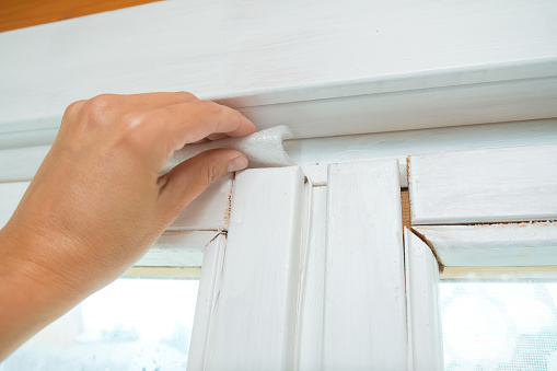 Woman hand insulating old windows to prevent warmth heat leak and drafts, preparing house for winter and cold weather.