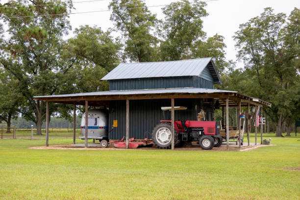 A tractor, fishing boat, and Airstream motor home sit under the shed roof of a painted wooden barn in a pecan orchard in rural Georgia, USA stock photo