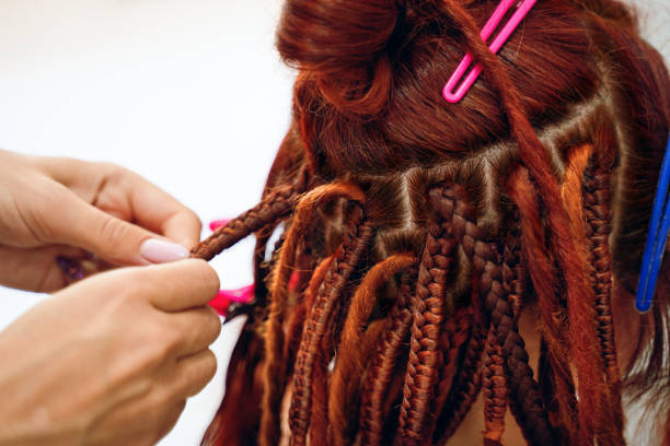 istock Hairdresser's hands braid girl's ginger dreadlocks. 1341746533