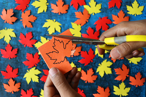 Stock photo showing an Autumn poster / background design with homemade cut out red, orange and yellow maple leaf shapes on blue crackle background, with copy space.