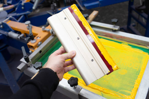 istock Squeegee for Serigraphy silk screen print process at clothes factory. Frame, squeegee and plastisol color paints 1341759705