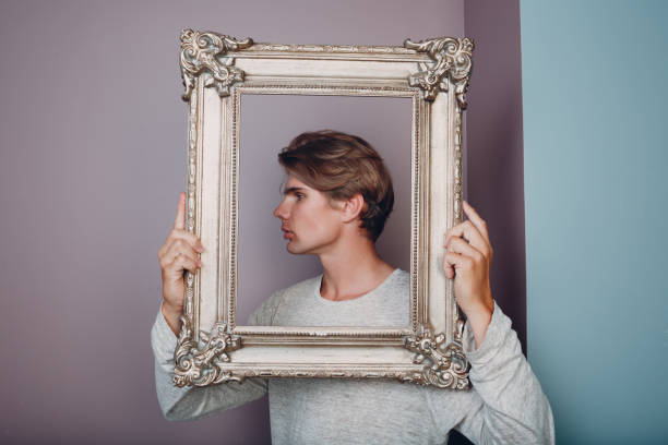 istock Portrait young man standing with picture frame at studio. 1341760239