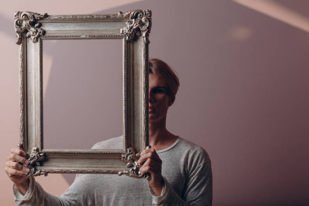 istock Portrait young man standing with picture frame at studio. 1341760306