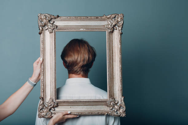 istock Portrait young man standing with picture frame at studio. 1341760335
