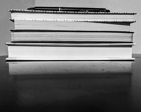 Black & white photo of a stack of books with a pen on top, reflected on a black table
