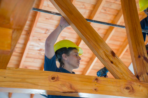 A female worker is drilling a wooden beam during wood frame house constructionn
