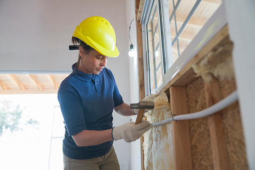 Female worker installing fiberglass insulation on wall during wood frame house construction