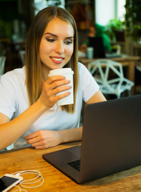 istock Happy young woman drinking coffee/tea and using laptop in a cof 1341765755