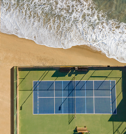 Drone view of tennis court by the sand and sea.