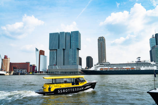 Water tax SS Rotterdam named for hotel of same name crosses harbor with cuise ship moored  in from of ultra-modern high-rise building De Rotterdam Rotterdam Netherlands - August 22 2021; Water tax SS Rotterdam named for hotel of same name crosses harbor with cruise ship moored  in from of ultra-modern high-rise building De Rotterdam. watertaxi stock pictures, royalty-free photos & images