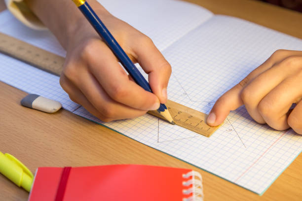 A student draws a line in a notebook with a pencil along a ruler.