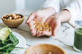 Woman doctor nutritionist hands in white shirt with omega 3, vitamin D capsules with green vegan food. The doctor prescribes a prescription for medicines and vitamins at the clinic, healthy food and treatment
