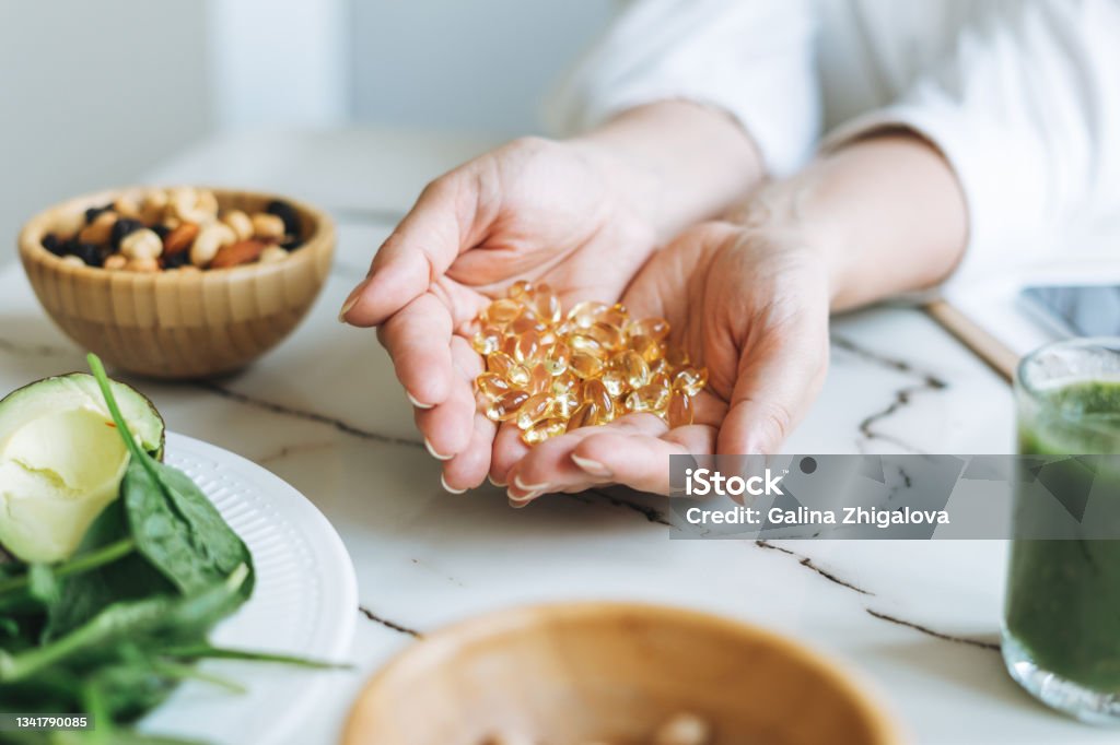 Woman doctor nutritionist hands in white shirt with omega 3, vitamin D capsules with green vegan food. The doctor prescribes a prescription for medicines and vitamins at the clinic, healthy food and treatment Woman doctor nutritionist hands in white shirt with omega 3, vitamin D capsules with green vegan food. The doctor prescribes a prescription for medicines and vitamins at clinic, healthy food and treatment Nutritional Supplement Stock Photo
