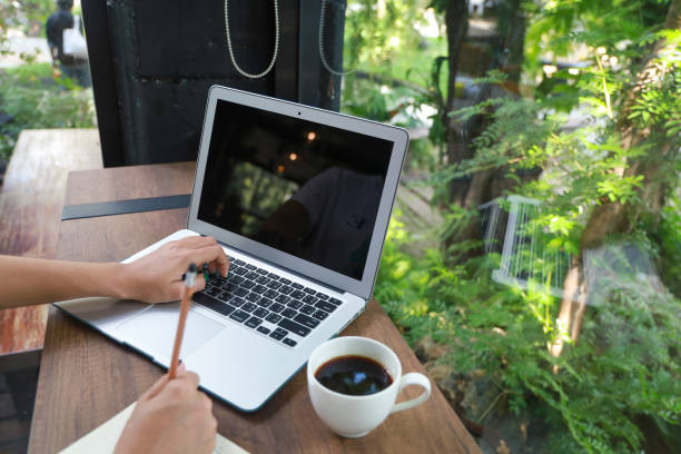 istock Women hand is working on a laptop. And note the notebook with a pencil. There is a cup of coffee beside the wooden table in the garden 1341791084