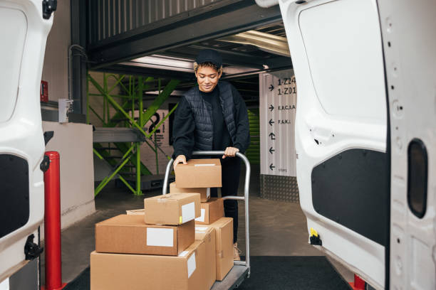 istock Woman in uniform checking cardboard boxes on a cart before putting them into a van while standing in a warehouse 1341796261