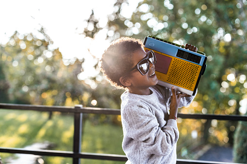 Cool black boy with sunglasses listening music over a radio on a balcony.