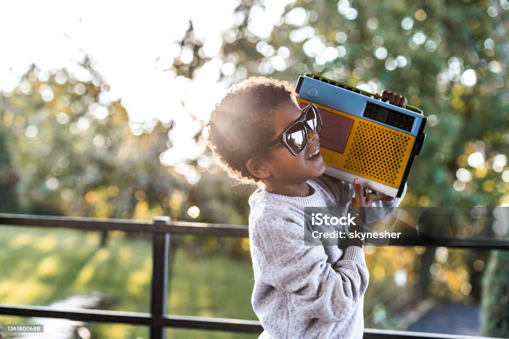 Cool African American boy with a radio on a terrace. Cool black boy with sunglasses listening music over a radio on a balcony. Radio Stock Photo