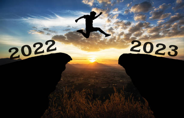 un joven salta entre 2022 y 2023 años sobre el sol y a través de la brecha de la silueta de la colina del cielo colorido. feliz año nuevo 2022. - intend fotografías e imágenes de stock