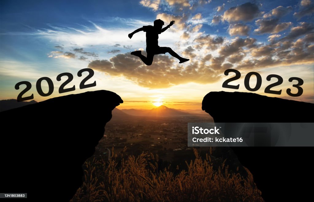 A young man jump between 2022 and 2023 years over the sun and through on the gap of hill  silhouette evening colorful sky. happy new year 2022. 2023 Stock Photo