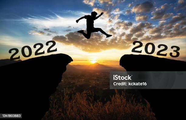 A Young Man Jump Between 2022 And 2023 Years Over The Sun And Through On The Gap Of Hill Silhouette Evening Colorful Sky Happy New Year 2022 Stock Photo - Download Image Now