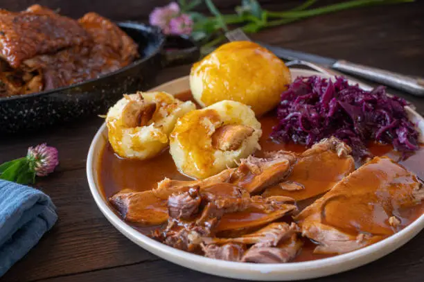 Delicious homemade meal with roast turkey and german potato dumplings served with a very tasty sauce and traditional red cabbage on a plate. Closeup view on wooden table.