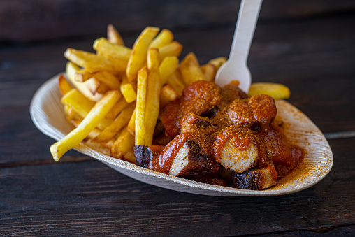 Traditional german currywurst with french fries served on a eco conscious and disposable plate. Closeup and isolated view on wooden table