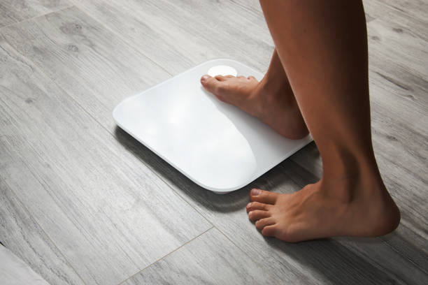 Female leg stepping on floor scales, close-up Female leg stepping on floor scales, close-up. Woman and weighing scales at home. Diet, healthy lifestyle, loss weight, slim concept. scales stock pictures, royalty-free photos & images