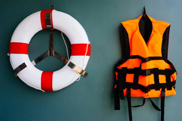 Orange life jacket and white-red life buoy hang on the wall together for keeping a person afloat in water