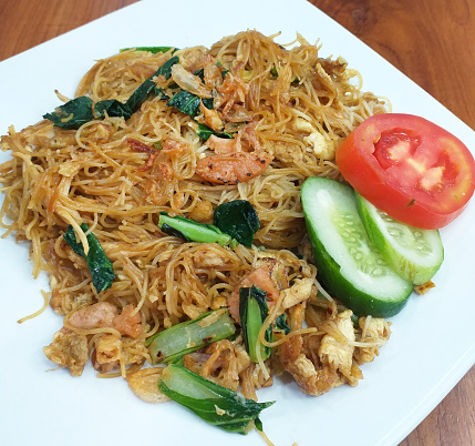 Fried rice noodles of bihun Goreng, a common dish in Indonesia and Southeast Asia with a garnish of sliced tomato and cucumber.