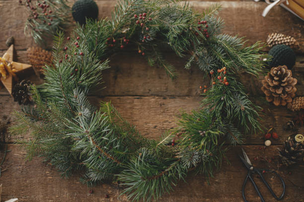 istock Christmas rustic wreath. Stylish christmas wreath on rustic wooden background with scissors, pine cones, candles, ornaments. Happy holidays. Festive winter workshop, making xmas wreath 1341824877