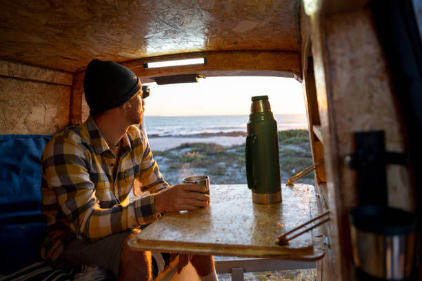 istock Man sitting inside camper van with hot drink and flask 1341829395