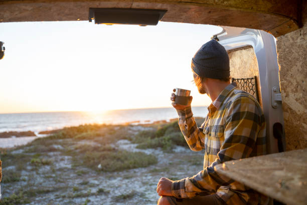 istock Man with travel mug looking at setting sun from camper van 1341829410