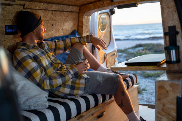 man relaxing in back of camper van looking at the view - hipster people surfing the net internet imagens e fotografias de stock