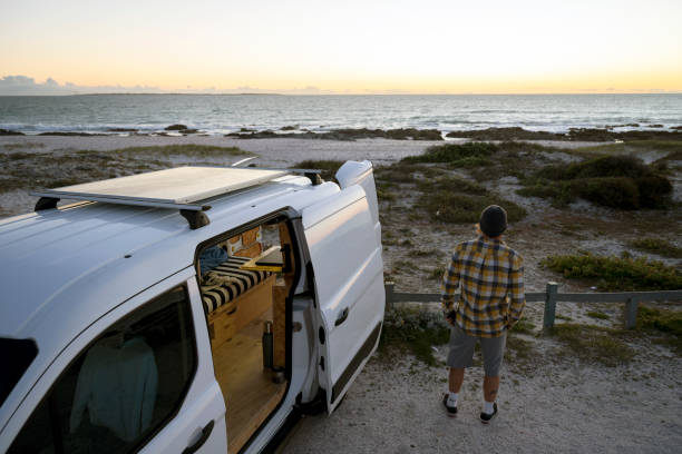 istock Man stands next to open camper van with solar panel looking out to sea 1341829453