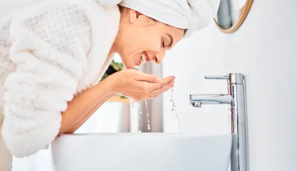 Photo of Shot of a young woman washing her face in her bathroom