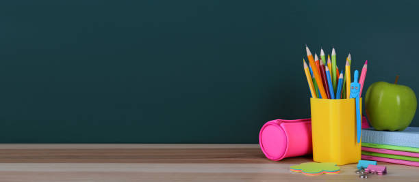istock Stationery and apple on table near chalkboard, space for text. Banner design 1341830568