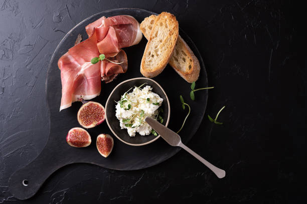 prosciutto crudo secco con fette di pane su fondo nero, prosciutto crudo all'antipasto italiano con frutta e formaggio. - delicatessen meat cold cuts chopped foto e immagini stock