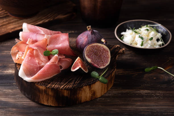 Prosciutto slices with figs on a dark wooden background, appetizer from dry cured ham. Prosciutto slices with figs on a dark wooden background, appetizer from dry cured ham, rustic style. prosciutto stock pictures, royalty-free photos & images