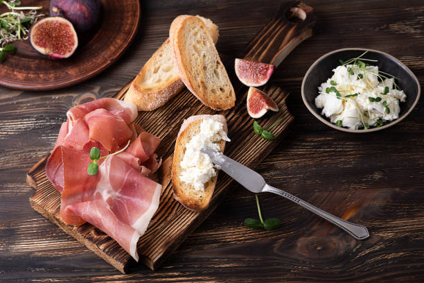 crostini com ricota, prosciutto e figos, antipasto italiano em um fundo de madeira escura. - delicatessen meat cold cuts chopped - fotografias e filmes do acervo