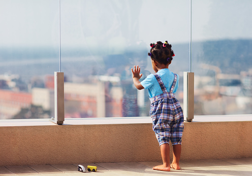 cute toddler baby watching the cityscape from the rooftop patio with glass balustrade