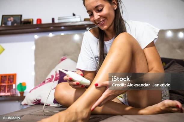 A Young Woman Epilating Her Legs At Home Stock Photo - Download Image Now - 25-29 Years, Adult, Adults Only