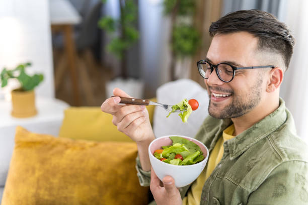 istock Young man eating a salad while relaxing on sofa. 1341836539